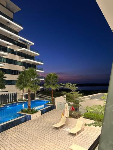 a swimming pool with two lounge chairs and a building at Beachside Sunset Residence in Abu Dhabi