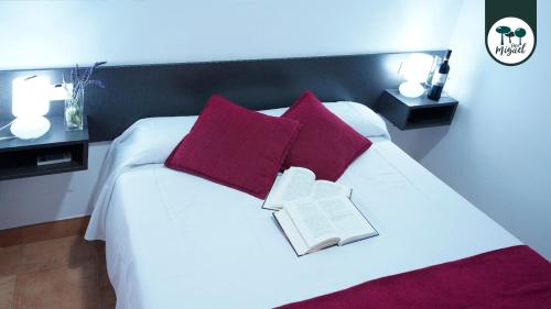 a bed with red pillows and a book on it at Hostal Rte. Casa Miguel in Matalascañas