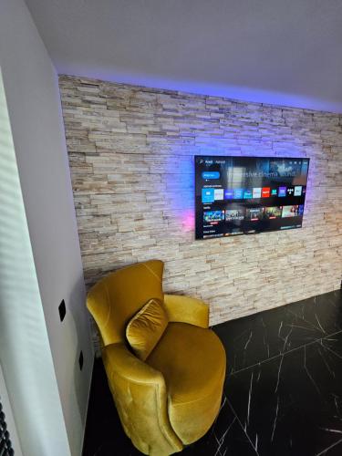 a yellow chair in front of a brick wall with a tv at Cristina Apartment in Râşnov