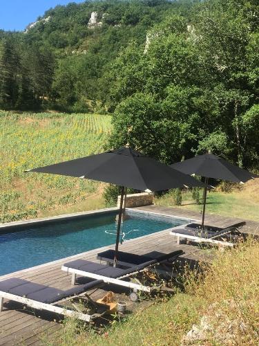 two umbrellas and lounge chairs next to a pool at Le Mas de Laval in Saint-Cirq-Lapopie