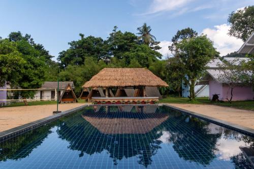 a swimming pool in front of a house with a thatch roof at Slumber Resort Koh Chang in Ko Chang