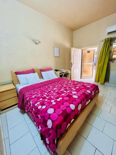 ein Schlafzimmer mit einem großen Bett und einer rosa Tagesdecke in der Unterkunft Hôtel Saint Thomas in Lomé