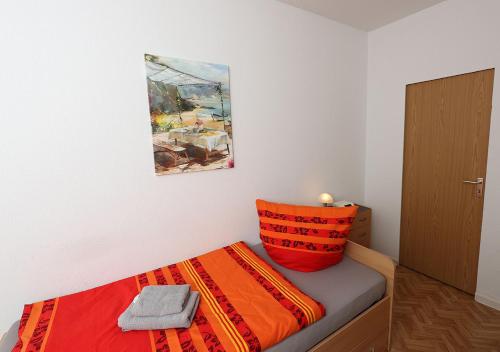 a bed with an orange pillow and a painting on the wall at Ferienwohnung Inselzoo der WAG in Altenburg