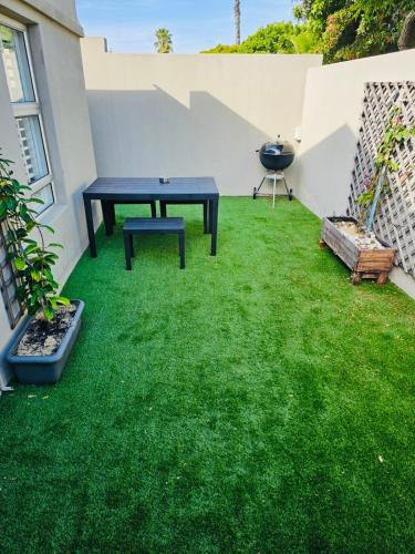 een patio met een tafel en groen gras bij Blouberg Rise Cottage in Kaapstad