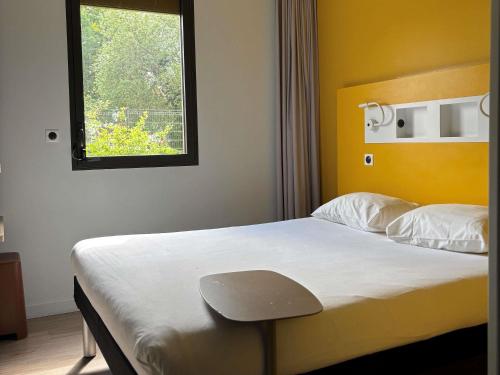 a bedroom with a bed with a yellow headboard and a window at ibis budget Rennes Rte Lorient in Rennes
