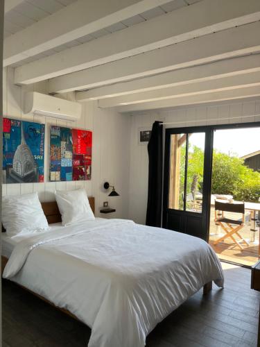 ein Schlafzimmer mit einem großen weißen Bett und einer Terrasse in der Unterkunft Chambre d'Hôtes - Village Petit Piquey in Cap-Ferret
