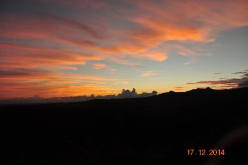 a sunset in a field with a hill in the background at Hawk's Nest Bed & Breakfast in La Laguna de San Carlos