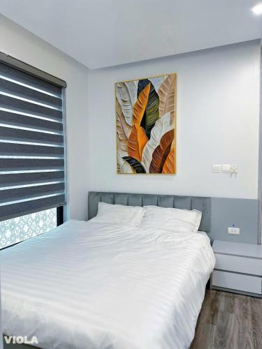 une chambre avec un lit blanc avec un tableau sur le mur dans l'établissement Viola Imperia Apart Charming Luxury 2Brs SwimPool, à Hanoï