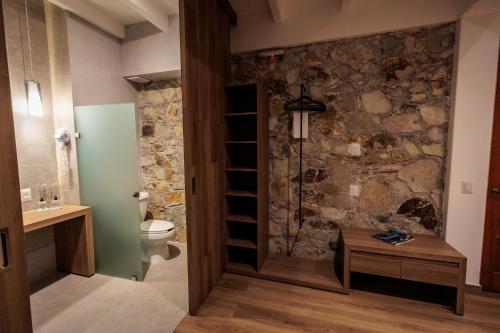 a bathroom with a toilet and a stone wall at Hotel Tabáa Oaxaca in Oaxaca City