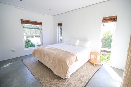 a white bedroom with a bed and two windows at Calm Oasis in the heart of the Karoo in Prince Albert