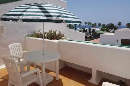 a table and a chair and an umbrella on a balcony at Bonito apartamento reformado en Las Coronas in Costa Teguise