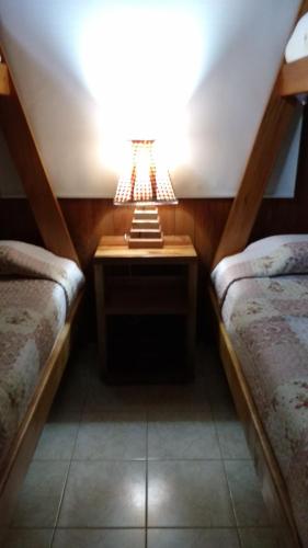 a room with two beds and a table with a lamp at Cabañas Tornagaleones Villarrica in Villarrica