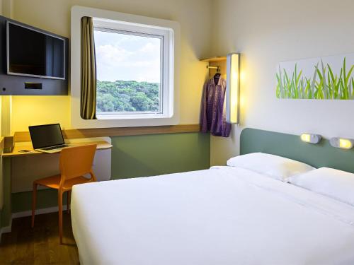 a bedroom with a bed and a desk and a window at ibis budget Curitiba Aeroporto in São José dos Pinhais