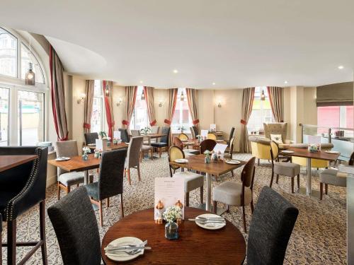 a restaurant with wooden tables and chairs and windows at Mercure Doncaster Centre Danum Hotel in Doncaster