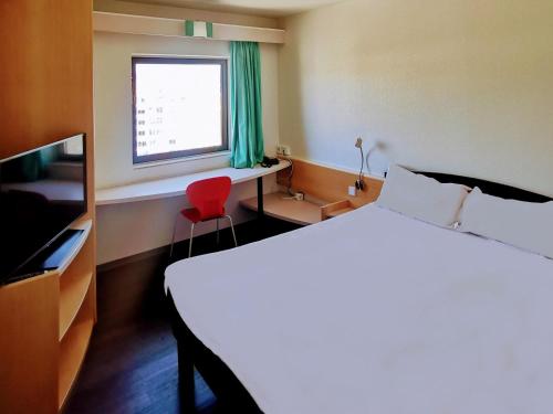 a bedroom with a bed and a window and a red chair at Hotel ibis Leiria Fatima in Leiria