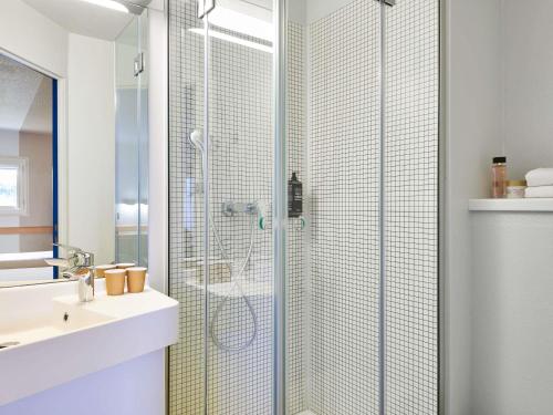 Un baño con ducha con puerta de cristal. en ibis budget Versailles Chateau Saint cyr l'Ecole, en Saint-Cyr-lʼÉcole