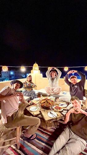 a group of people sitting around a table with food at Riad Dar Sahara - Panoramic Rooftop & Outdoor Shower in Nkob