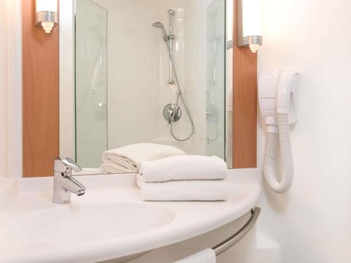 a bathroom with a sink with a shower and towels at Ibis Vitré Centre in Vitré