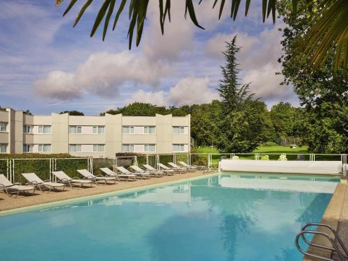 a large swimming pool with lounge chairs and a building at Novotel Fontainebleau Ury in Ury