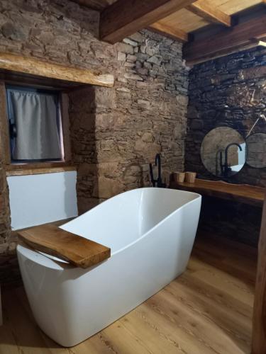 una vasca da bagno bianca in una stanza con parete in pietra di Linhares - Country House Turismo, Natureza e Aventura a Castanheira de Pêra