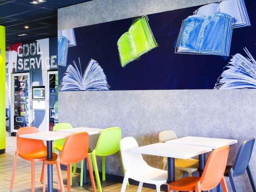 a restaurant with white tables and colorful chairs at ibis budget Bergerac in Bergerac