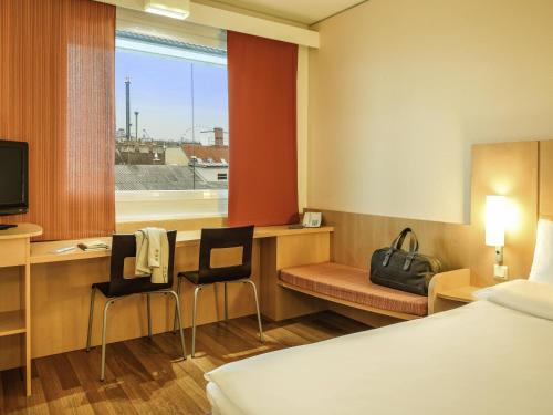 a hotel room with a desk and a bed and a window at Ibis Wien Messe in Vienna