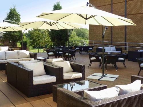a patio with chairs and tables and an umbrella at Mercure Milton Keynes Hotel in Milton Keynes