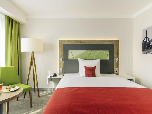 a hotel room with a large bed and a green chair at Mercure Hotel Saarbrücken City in Saarbrücken