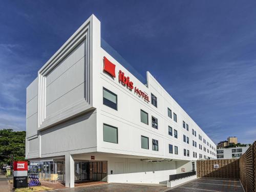 a large white building with a red sign on it at ibis Chiang Mai Nimman Journeyhub in Chiang Mai