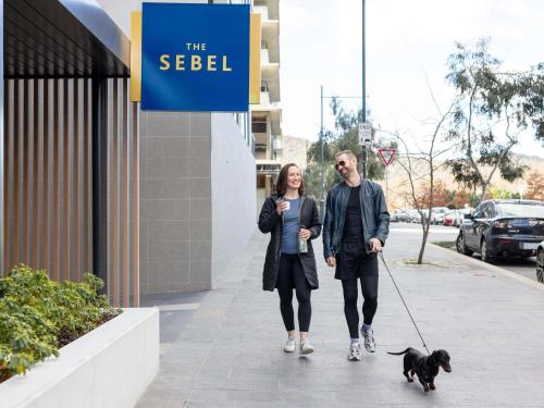 a man and a woman walking a dog on a sidewalk at The Sebel Canberra Campbell in Canberra