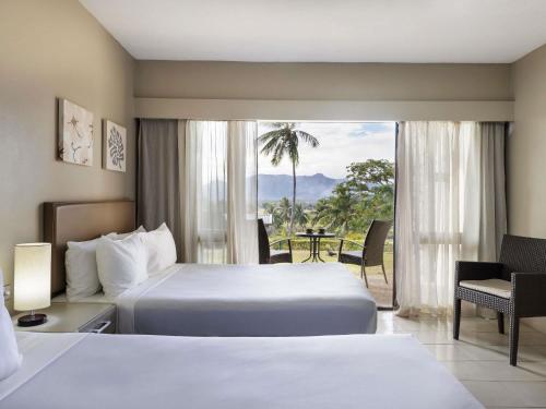 a hotel room with two beds and a balcony at Novotel Nadi in Nadi