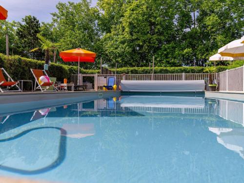 a swimming pool with an umbrella and some chairs and tables at Mercure Reims Parc Des Expositions in Reims