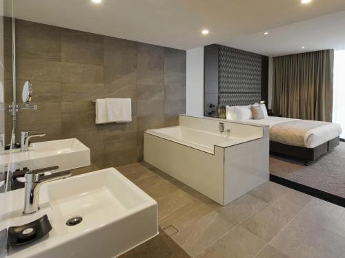 a bathroom with a tub and a sink and a bed at Pullman Brisbane Airport in Brisbane