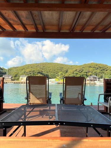 a table and chairs on a deck with a view of the water at Guest House & Cafe Yamaboushi in Tsushima