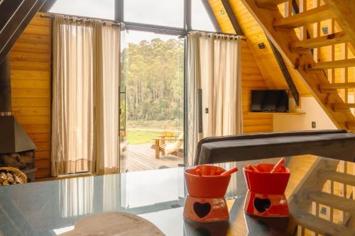 a room with a glass table with two red vases at Chalés Sol da Serra - Eucalipto in Rio Rufino
