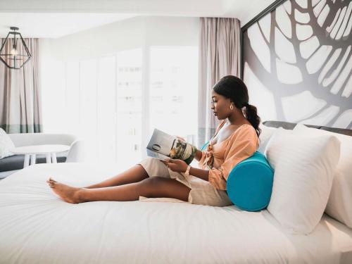 a woman sitting on a bed reading a book at Pullman Cairns International in Cairns