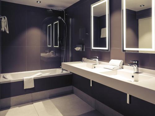 a bathroom with two sinks and a tub and mirrors at Hotel Mercure Blois Centre in Blois