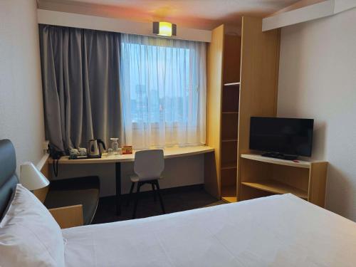 a hotel room with a bed and a desk with a television at Ibis Katowice - Zabrze in Zabrze