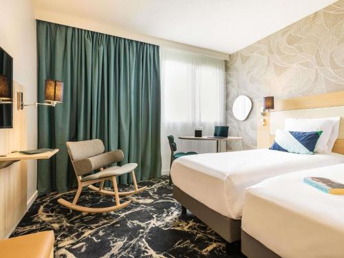 a hotel room with two beds and a chair at Mercure Mulhouse Centre in Mulhouse