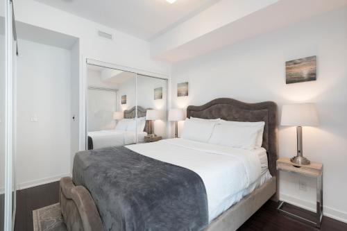 a white bedroom with a large bed and a mirror at Luxury 1BR Suite - Lake & City View on 39th Floor in Toronto