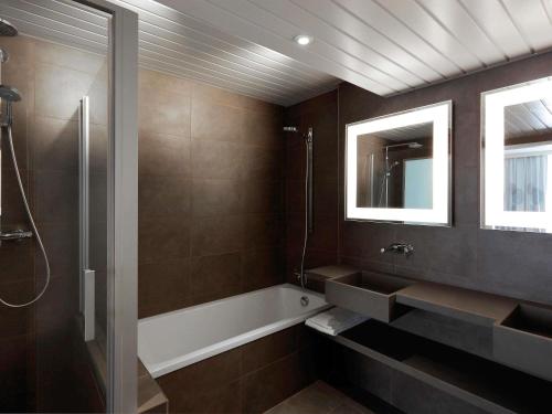 a bathroom with a tub and a sink and a mirror at Novotel Narbonne Sud A9/A61 in Narbonne
