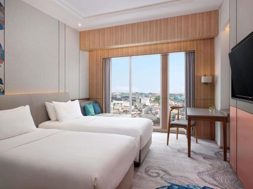 a hotel room with two beds and a desk and a window at Mercure Samarinda in Samarinda