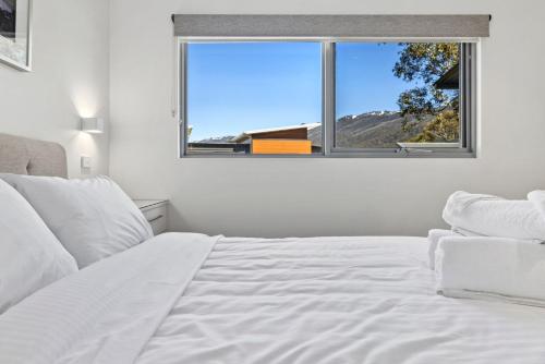 Un dormitorio con una cama blanca y una ventana. en Little Rocky Retreat, en Perisher Valley