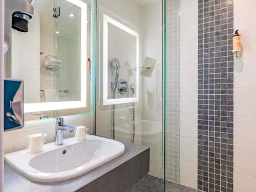 Un baño con lavabo y ducha de cristal. en Mercure Lyon Est Villefontaine, en Villefontaine