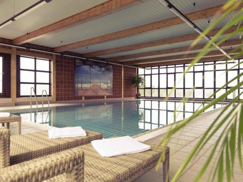a swimming pool with two chairs in a building at Mercure Hotel am Messeplatz Offenburg in Offenburg