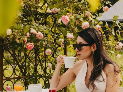 een vrouw aan een tafel die een kop koffie drinkt bij Hotel de L'Abbaye Le Tronchet - Handwritten Collection in Le Tronchet