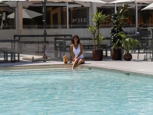 a woman in a white bikini sitting next to a swimming pool at Novotel Montpellier in Montpellier