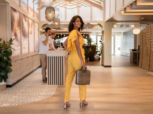 a woman in a yellow suit walking down a hallway at Novotel Montpellier in Montpellier
