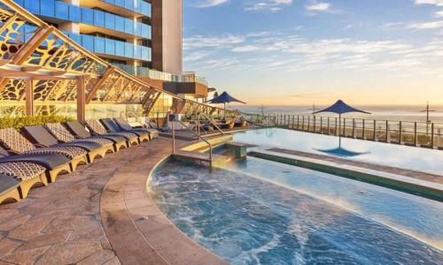 a hotel with a pool and chairs and the ocean at Soul Beachfront Apartments - Hosted by Coastal Letting Co. in Gold Coast