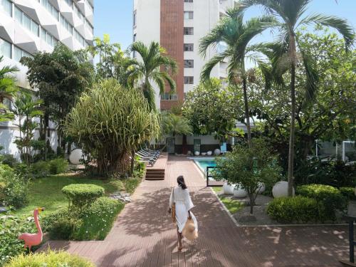 uma mulher caminhando por uma passarela em um parque com palmeiras em Novotel Abidjan Plateau em Abidjan